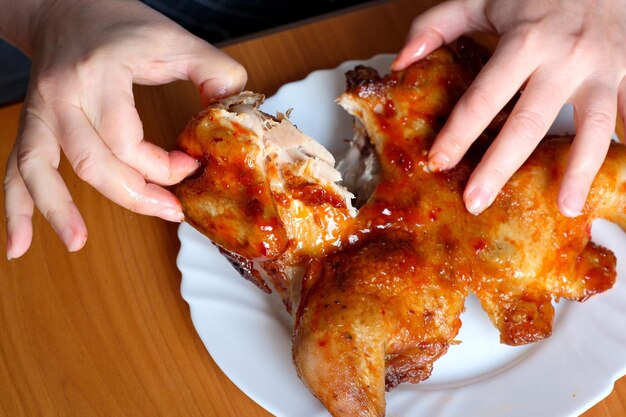 De handen van een oudere vrouw bedienen een gegrilde kip en tonen deze in de keuken aan een bruine tafel zonder gezichtsclose-up