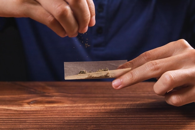 De handen van een persoon die een joint in elkaar zet en cannabisbloemen van bovenaf draagt