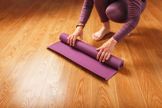 De handen van een vrouw leggen een lila yoga- of fitnessmat neer voor een training thuis op een houten vloer