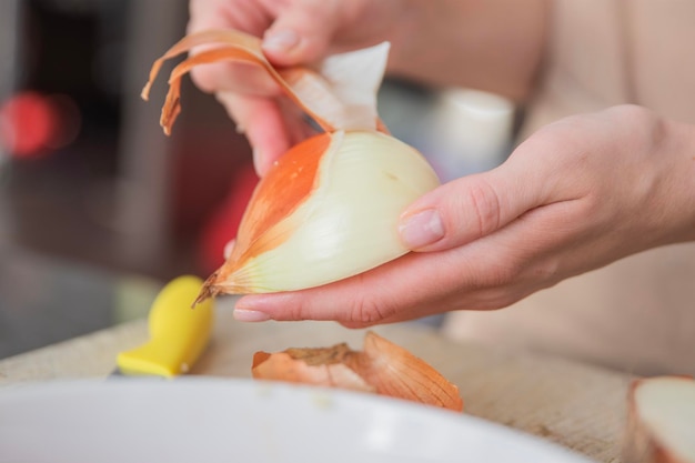 De handen van een vrouw schillen een ui in plakjes close-up het proces van het koken van uien als dressing
