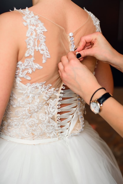 De handen van het bruidsmeisje maken knopen op de rug van de bruid op de trouwjurk vast
