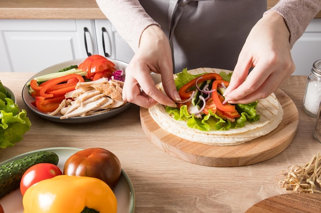 De handen van het jonge meisje leggen netjes de ingrediënten op gegrilde flatbreads het proces van het maken van tortilla's met groenten en kip