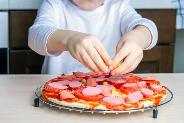 De handen van het kind strooien kaas op pizzadeeg. Proces om zelfgemaakte pizza door kind te koken. Kleutervaardigheden, kleine helper. Familie-vrije tijd. Kunstmatig geluid, selectieve focus, tegenlicht
