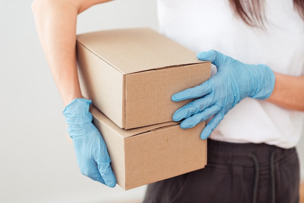 De handen van het meisje in handschoenen houden twee kleine dozen vast, verzenden en verpakken van het pakket, veilige levering