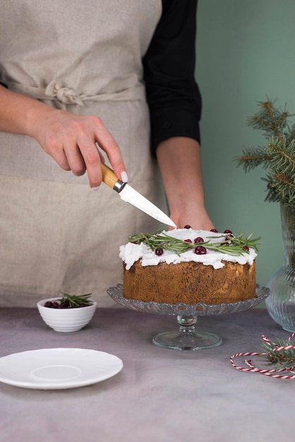 De handen van het meisje snijden de kersttaart met rode bessen op een grijze tafel