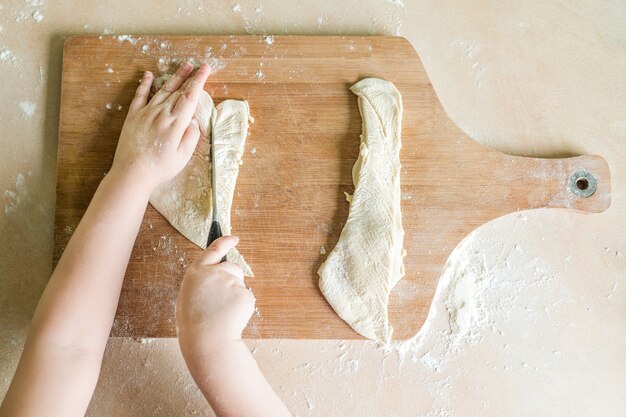 De handen van kinderen die ruw deeg snijden