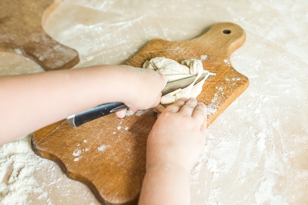 De handen van kinderen die ruw deeg snijden