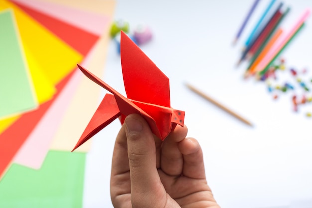 Foto de handen van kinderen doen origamivogel van rood document