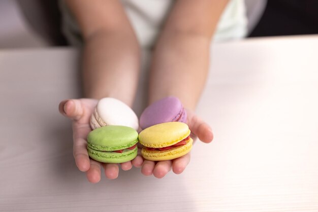 De handen van kinderen houden macarons op een witte achtergrond, traditioneel Frans veelkleurig macaronvoedsel