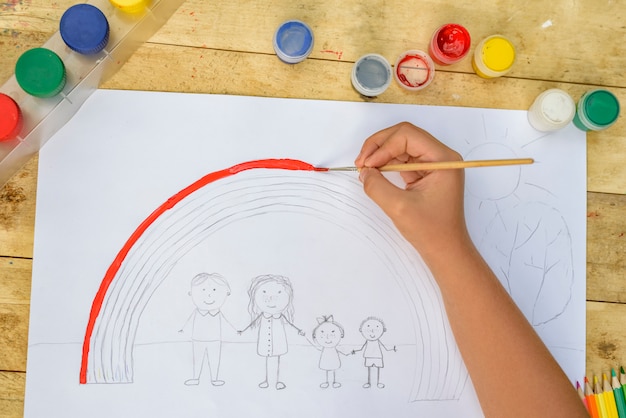 De handen van kinderen schilderen een tekening met een penseel en verf. Bovenaanzicht