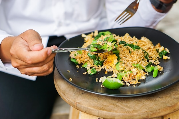 De handen van mannen eten lepel puree Thaise Pat gebakken noedels en groenten in zwarte schotel