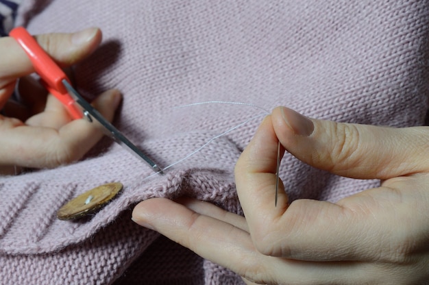 Foto de handen van vrouwelijke arbeiders naaien een houten knoop aan een jas. detailopname.