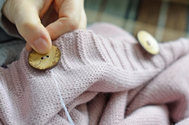 De handen van vrouwelijke arbeiders naaien een houten knoop aan een jas. detailopname.