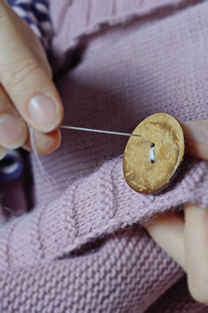 Foto de handen van vrouwelijke arbeiders naaien een houten knoop aan een jas. detailopname.