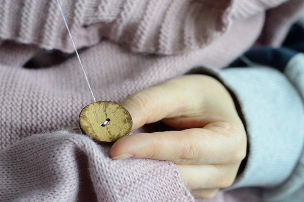 De handen van vrouwelijke arbeiders naaien een houten knoop aan een jas. detailopname.