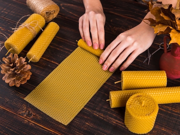 De handen van vrouwen maken handgemaakte kaarsen van natuurlijke was met textuur van honingraatbijen, op een houten tafel.