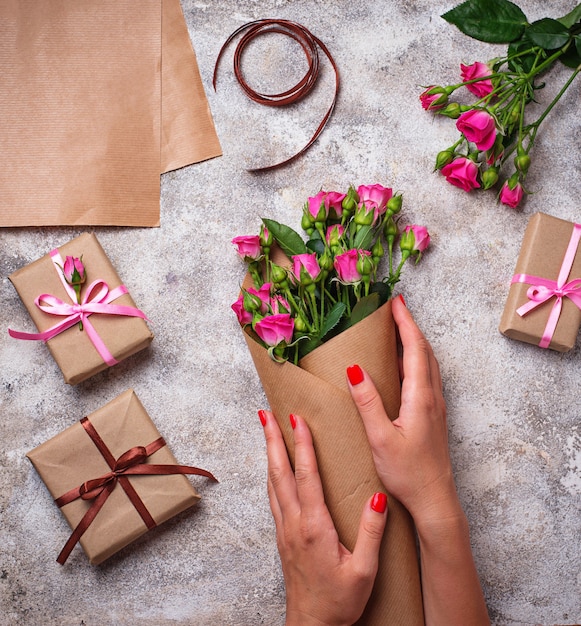 De handen van vrouwen wikkelen een boeket rozen in papier