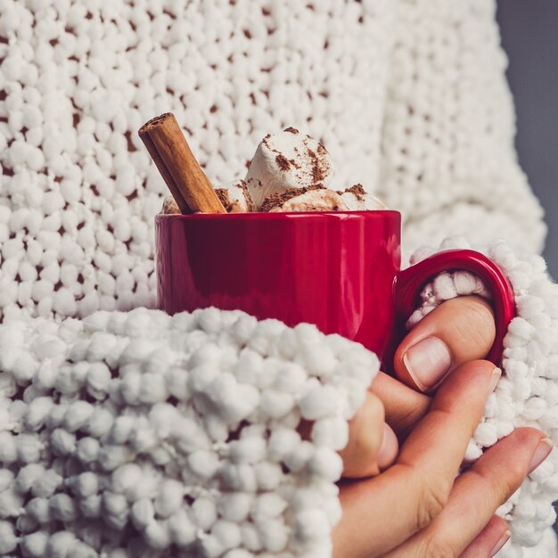 De handen van vrouwen, witte sweater en rode mok