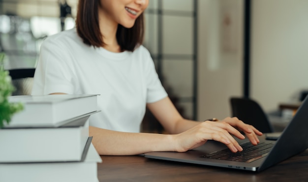 De handholding van de vrouw drukt op de knoop op toetsenbordlaptop en stapel boeken.