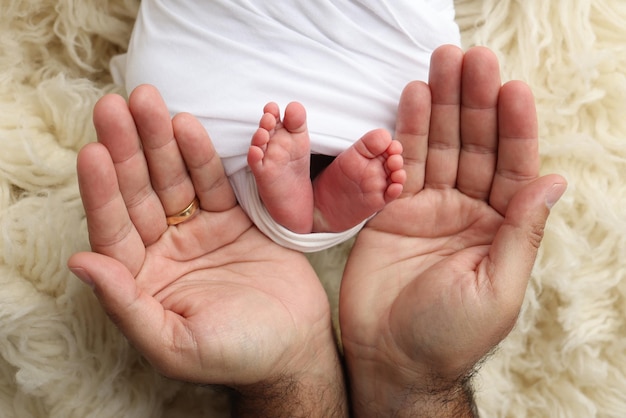 De handpalmen van de vader de moeder houden de voet van de pasgeboren baby in een witte deken de voeten van de nieuwgeboren baby op de handpalms van de ouders Studio macro foto van de tenen, hielen en voeten van een kind