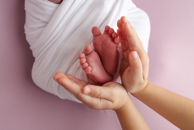 De handpalmen van de vader de moeder houden de voet van de pasgeboren baby in een witte deken de voeten van de nieuwgeboren baby op de handpalms van de ouders Studio macro foto van de tenen, hielen en voeten van een kind