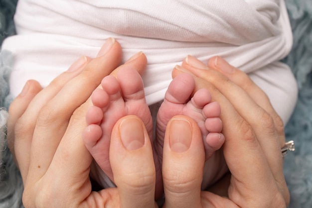 De handpalmen van de vader, de moeder houden de voet van de pasgeboren baby vast in een witte deken. Voeten van de pasgeborene op de handpalmen van de ouders. Fotografie van de tenen, hielen en voeten van een kind.