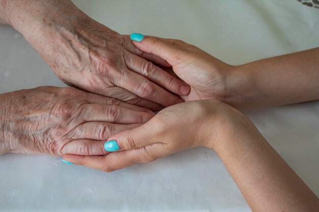 De handpalmen van een jong meisje houden de handen van een oudere vrouw op een wit tafelkleed
