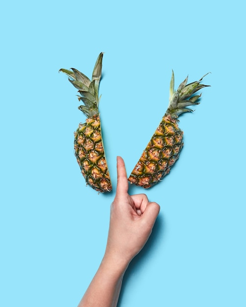 De helft van de ananas en de vinger van de vrouwelijke hand snijdt fruit op een blauwe achtergrond met ruimte voor tekst