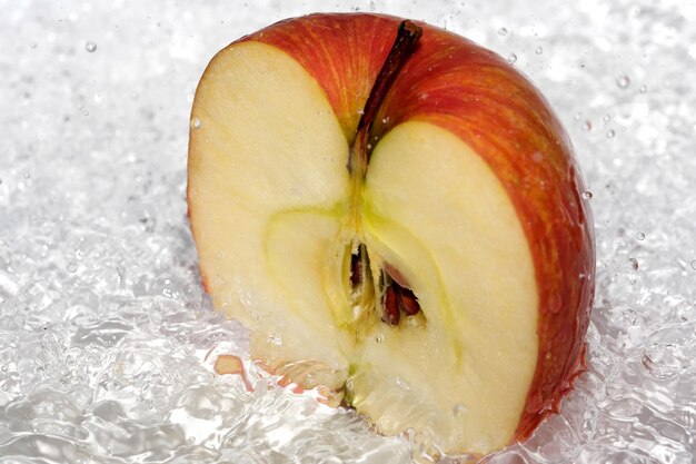 De helft van een rode rijpe zoete appel op een witte plaat wordt gegoten met water uit een douche die fruit close-up macro fotografie reinigt