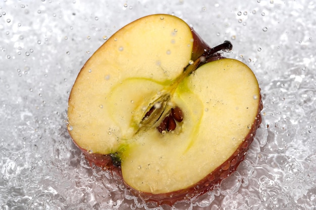 De helft van een rode rijpe zoete appel op een witte plaat wordt gegoten met water uit een douche die fruit close-up macro fotografie reinigt