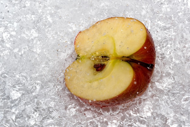 Foto de helft van een rode rijpe zoete appel op een witte plaat wordt gegoten met water uit een douche die fruit close-up macro fotografie reinigt