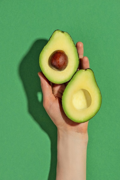 De helft van een verse rijpe avocado in een vrouwelijke hand op een groene achtergrond