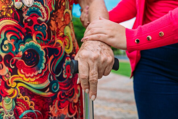 De helpende handen voor wandelstok bejaarde vrouw thuiszorg in een park buiten.