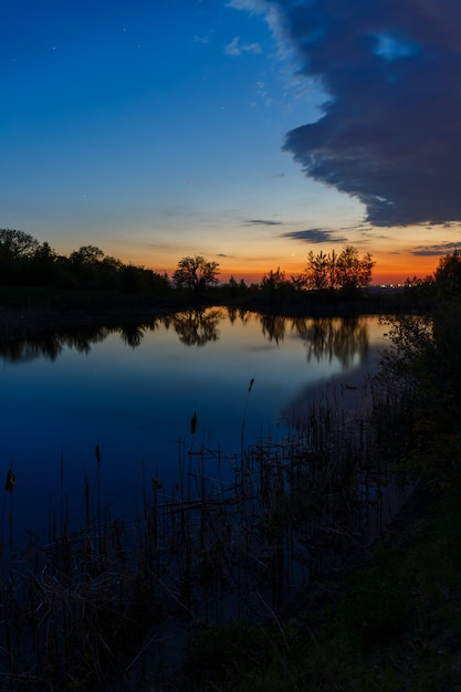 De hemel met heldere wolken verlicht door de zon na zonsondergang over het meer