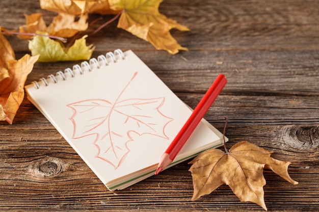 De herfstachtergrond met bladeren van esdoorn en Eikels a op houten achtergrond. papier met een potlood in de herfst achtergrond, plaats voor tekst