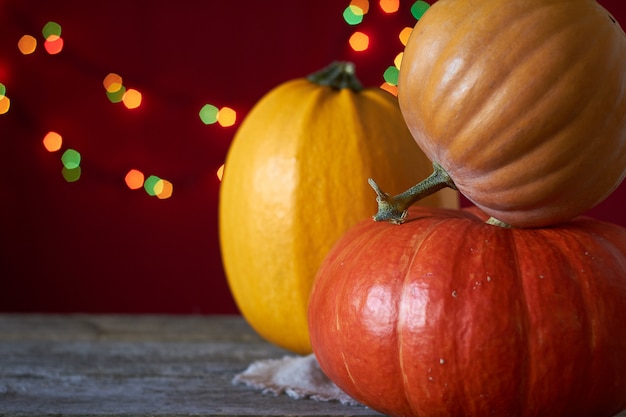 De herfstachtergrond op een donkere houten oppervlakte, drie pompoenen op een achtergrond van wazige lichten