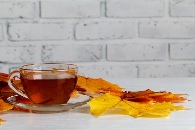 De herfstbladeren en hete stomende kop thee op houten oppervlakte