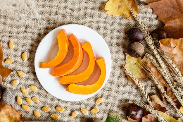 De herfstpompoen, esdoornbladeren en kastanjes die op een bruin liggen.