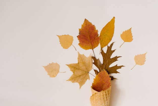 De herfstroomijs met gevallen gele bladeren in een wafelkop op een beige achtergrond. herfst menu concept. plat leggen en kopiëren