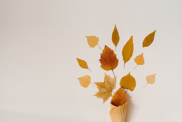 De herfstroomijs met gevallen gele bladeren in een wafelkop op een beige achtergrond. Herfst menu concept.