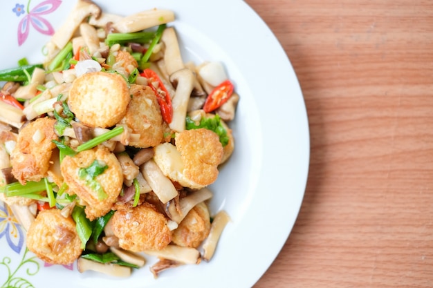 Foto de hete geroerbakte tofu en het varkensvlees en de paddestoel met zwarte bonensaus dienen op witte schotel die op bruine lijst wordt geplaatst - eigengemaakt voedselconcept.