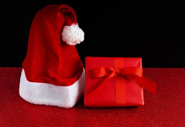 De hoed van de kerstman en een rode geschenkdoos op een glitterachtergrond