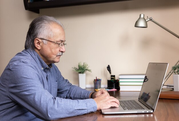 De hogere mens leert computer te gebruiken. Oude man in glas en blauw shirt met behulp van een laptopcomputer voor online studeren thuis kantoor