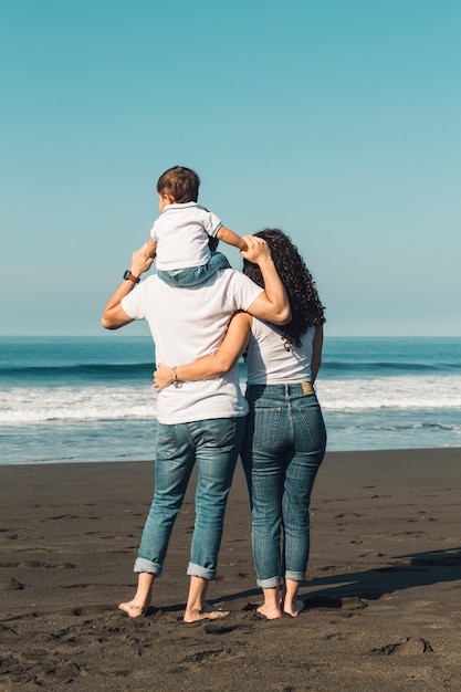 Foto de holdingsbaby van de vader op hals en het koesteren met vrouw op strand