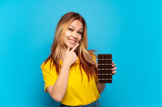 De holdingschocolat van het tienermeisje over geïsoleerde blauwe gelukkige en glimlachende achtergrond