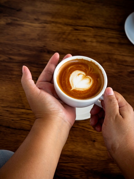 De holdingskop van het meisje van koffie latte op houten lijst