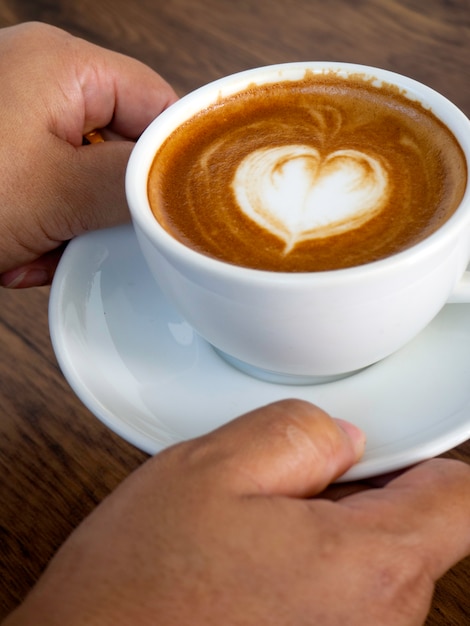 De holdingskop van het meisje van koffie latte op houten lijst