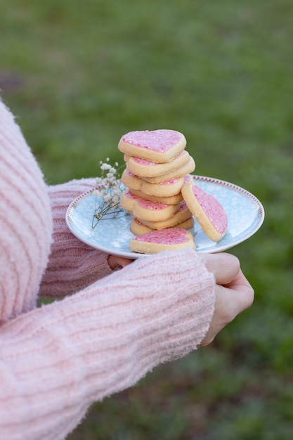 De holdingsplaat van het meisje met roze hart gevormde koekjes