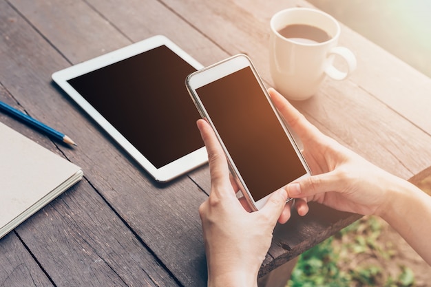 De holdingstelefoon van de vrouwenhand en het gebruiken van telefoon op lijst in tuin bij koffiewinkel met gestemde wijnoogst.