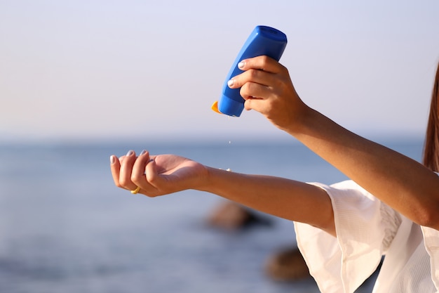 De holdingszonnescherm van de vrouwenhand op het strand met het overzees op blauwe hemelachtergrond, spf sunblock bescherming en het concept van de huidzorg